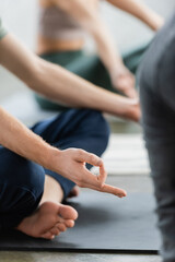 Obraz na płótnie Canvas Cropped view of man doing gyan mudra on mat in yoga class.