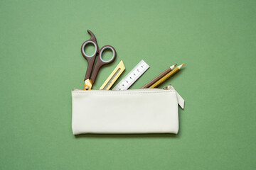 School office writing supplies in pencil case on green desk. top view, copy space