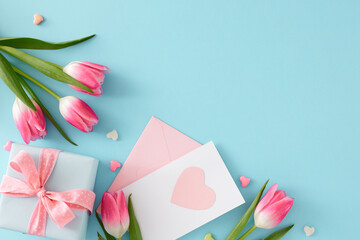 Women's Day atmosphere concept. Flat lay photo of gift box with bow postcard hearts baubles pink tulips flowers on isolated pastel blue background with copyspace