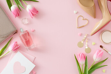 Top view photo of trendy woman shoes perfume bottle cosmetics handbag postcard and pink tulips on pastel pink background with empty space in the middle. Mother's Day concept
