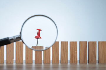 A magnifying glass magnifies the pin pierced into the wooden blocks