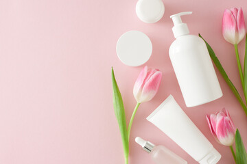 Organic skincare concept. Flat lay photo of cosmetic tubes without label cream jar pump bottle and pink tulips on isolated pastel pink background with copy space