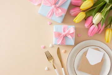 Mother's Day concept. Top view photo of gift boxes plate with envelope cutlery knife fork colorful hearts and yellow pink tulips on pastel beige background with empty space