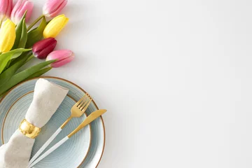 Mother's Day mood concept. Top view photo of circle plate with cutlery and fabric napkin with gold ring and bouquet of flowers yellow pink tulips on white background with empty space © Goncharuk film