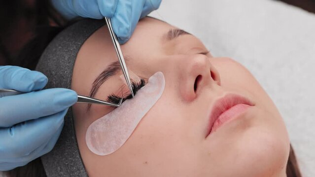 Eyelash extension procedure. The working process of professional beauty master lengthening female lashes. Fake eyelashes. Eyelashes extensions close up. Makeup artist and client in beauty salon