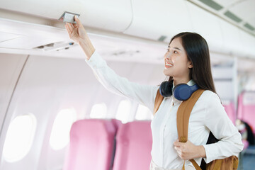 Young asian attractive woman travel by airplane, Passenger wearing headphone putting hand baggage...