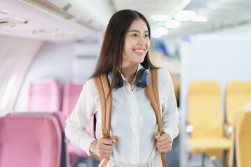 Young asian attractive woman travel by airplane, Passenger wearing headphone putting hand baggage in lockers above seats of plane