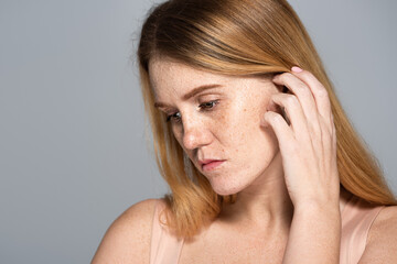 Upset woman with freckled skin looking away isolated on grey.