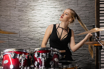 Fototapeta na wymiar Young cute blonde girl in wireless earphones sitting by the drums in a garage. female drummer. musician.