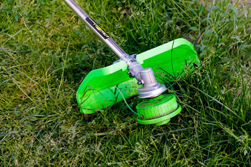 Defocus grass trimmer. A man mowing the grass. Outdoor view of a lawn trimmer mower cutting grass in a blurred nature background. Housework. Cutter edger. Out of focus