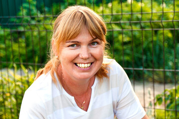 Portrait of smiling mature woman wearing stripe shirt and looking at camera. Summer green nature...