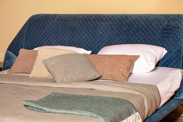 Folding soft sofa with quilted blue velor headboard and soft pillows in the interior of the bedroom.