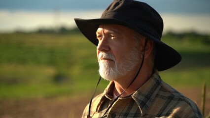 Close up portrait of senior caucasian good looking wise man farmer in a hat looking at the side,...