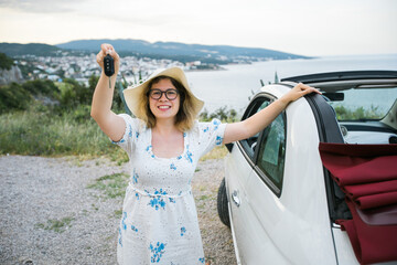Woman in summer hat driver holding car keys driving her new car cabriolet - automobile and purchase...