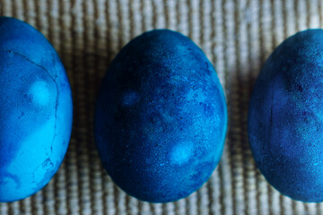 Line of three blue dyed easter eggs on woven backgroun