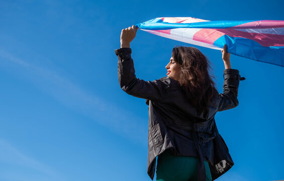 Transgender woman raising the trans flag in flight with a clear sky in the background. LGTBIQ+ activism