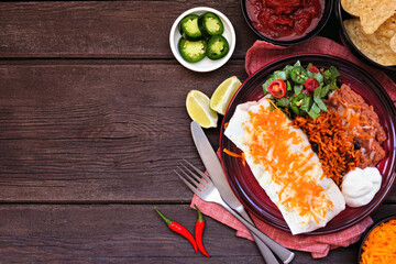 Burrito plate with Mexican rice and refried beans. Above view table scene on a dark wood background...