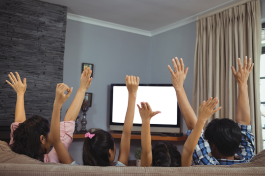 Rear view of family with arms raised watching television on sofa in living room