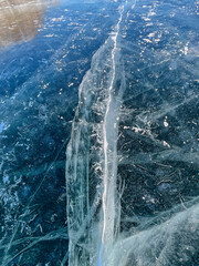 Fototapeta premium The natural texture of winter ice with white bubbles and cracks on a frozen lake. Abstract background of ice and cracks on the surface of frozen Lake Baikal