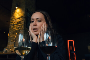 Attractive Caucasian woman looking on glasses of red and white wine in restaurant in the evening