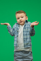 A kid boy shows a don't know gesture against on green background.