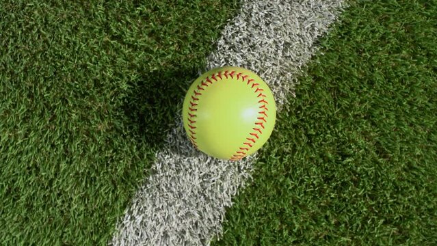 An overhead shot of a softball sitting on the foul line of the outfield grass as the camera rotates – slow.
