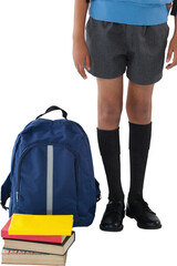 Low section of schoolboy standing by schoolbag and books