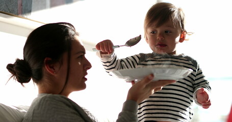 Funny baby toddler feeding mother reversing the roles. Adorable child feeds mom food