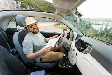 Hipster man looking on location navigation map in car, tourist traveler driving and hold in male...