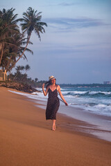 Happy young woman in beachwear lies walking on sandy beach at tropical background, summer vacation. Lady tourist in polka dot dress relaxing on seacoast. Travel rest holiday concept. Copy text space