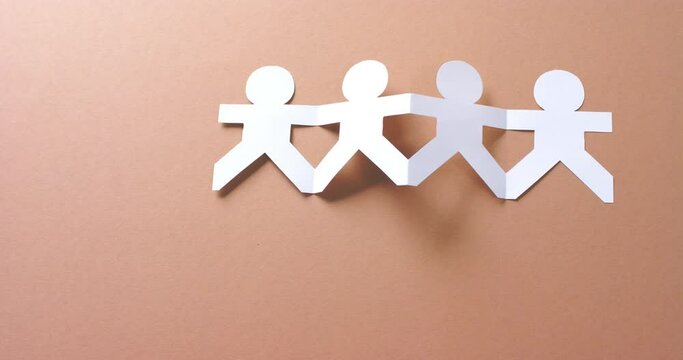 Close up of people holding hands made of white paper on beige background with copy space