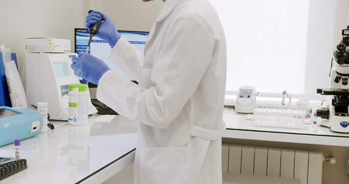 Male doctor analyzing samples in lab. Handheld shot of man in white robe with gloves and glasses putting vial with sample into machine during work in medical laboratory in clinic.