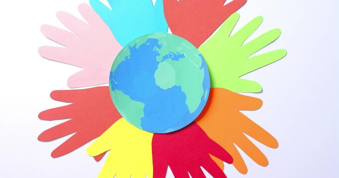 Close up of hands together with globe made of colourful paper on white background with copy space