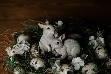 Two little easter bunny babies sitting on the wooden vintage table in the middle of an easter green wreath with herbs and eggs