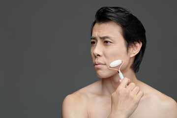 Frowning Asian man massaging face with roze quartz roller © DragonImages