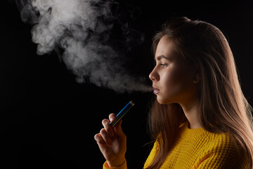 Obraz premium young girl smokes a vape close-up on a dark background