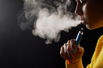 Fototapeta premium young girl smokes a vape close-up on a dark background