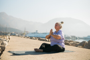 Mindful senior woman with dreadlocks meditating by the sea and beach copy space - wellness and yoga practice