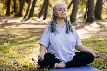 Mindful senior woman with dreadlocks meditating on nature - wellness and yoga practice - obrazy, fototapety, plakaty