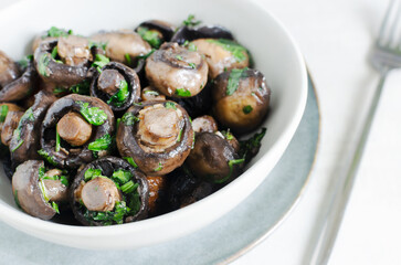 Fried champignons with garlic and parsley in a gray bowl. Vegetarian lifestyle concept. Horizontal orientation. Selective focus.