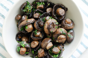 Fried champignons with garlic and parsley in a white bowl on the table. The concept of vegetarian food. Horizontal orientation. Selective focus. Top view.