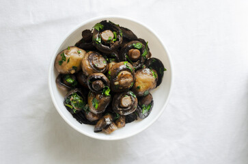 Fried champignons with garlic and parsley in a white bowl on the table. The concept of vegetarian food. Horizontal orientation. Selective focus. Top view.