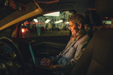 Fototapeta na wymiar woman senior female work on laptop computer in car at night in dark