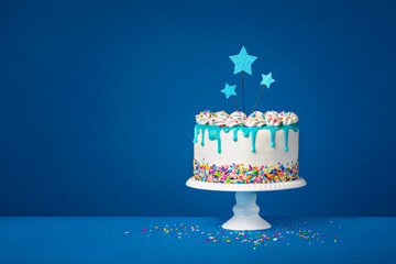 White birthday drip cake with teal ganache, star toppers over dark blue background - 588462861