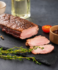 Grilled BBQ duck breast in marinade and spices with sauce on a slate board with fresh herbs on a dark background.
