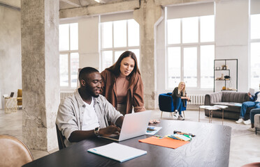 Cheerful multiethnic colleagues discussing project while working on laptop