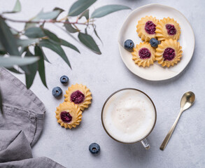 Cappuccino or latte with milk foam in a cup with  homemade berry cookies and blueberries on a light background with eucalyptus branches. Concept spring morning breakfast.