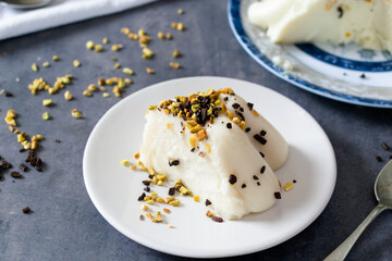 Biancomangiare, a traditional Sicilian vanilla pudding, garnished with chopped pistachios and chocolate, on dark background