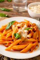 Pasta with tomato sauce, Parmesan cheese and basil, penne pomodoro, a classic Italian dish on a white plate and wooden table.