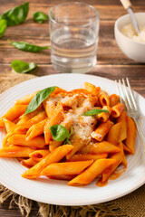Pasta with tomato sauce, Parmesan cheese and basil, penne pomodoro, a classic Italian dish on a white plate and wooden table.